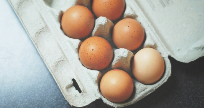Several brown eggs in a cardboard egg carton on a dark countertop